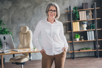Photo of positive aged lady company founder put hands pockets posing spacious workstation indoors