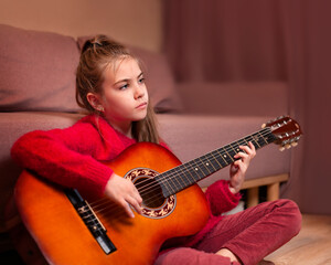 teen girl playing guitar sitting on the floor