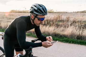 Male cyclist dressed in black leaning on the handlebar while checking his location or the map on...
