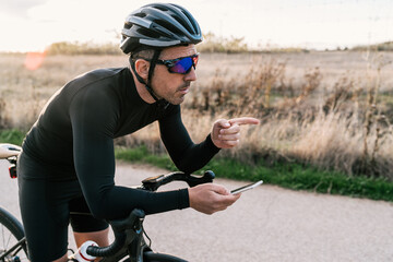 Male cyclist dressed in black leaning on the handlebar while checking his location or the map on...