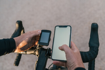 Hands of a cyclist dressed in black leaning on the handlebar synchronizing his mobile phone with...