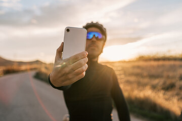 Cyclist man dressed in black taking a vertical selfie with his cell phone at sunset.