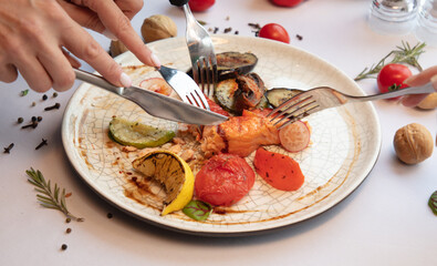 Hands with forks on a plate red fish with vegetables
