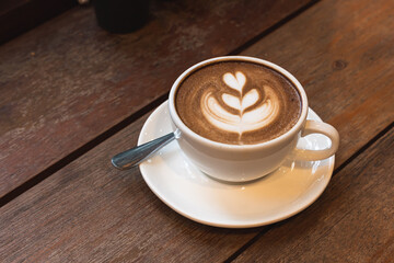 Hot coffee latte with latte art milk foam in cup mug on wood desk on top view. As breakfast In a coffee shop at the cafe, during business work concept