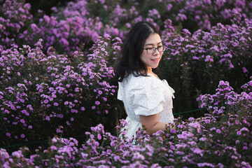Portrait of asian Young woman happy traveler with white dress enjoying in white blooming or purple Michaelmas Daisy flower field in the nature garden of in Chiang Mai,Thailand,travel relax vacation