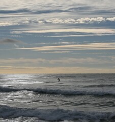 Fondo con detalle de persona practicando paddelsurf  con olas y cielo con nubes