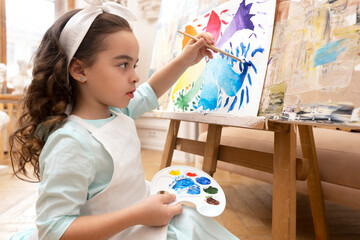 Cute girl drawing with a paint palette and a paintbrush. Little painting artist.