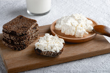 Rye bread on a wooden cutting board with curd cheese and milk