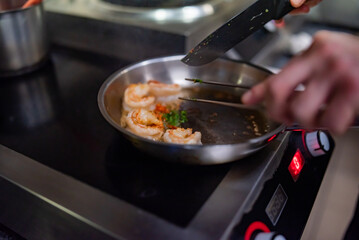 man chef cooking tasty shrimp in frying pan on kitchen