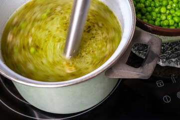 Stick blender blends soup in pot on hob, pea.