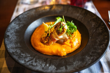 Zander fillet with bacon on pumpkin puree, rucola leaf in black plate.