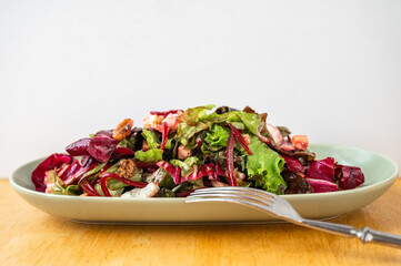 Red and green salad, sliced beetroot, tofu cube and walnut on oval plate, fork.