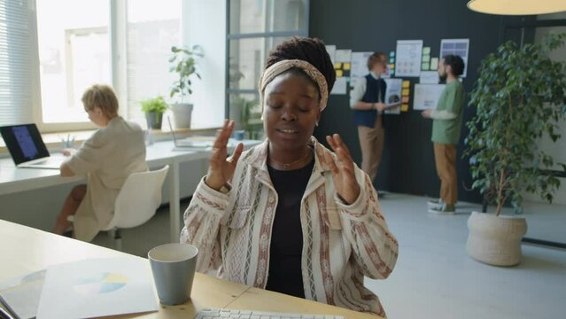 Young black businesswoman showing printed financial graph on camera and explaining it while discussing project via online video call during office workday