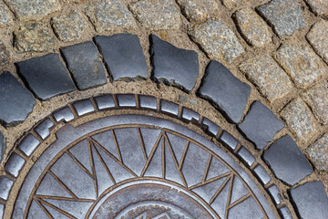 Old metal sewer hatch in the middle of the road, laid out of a smooth paving stone