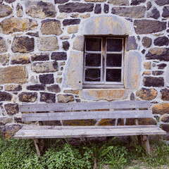 Fototapeta na wymiar banc en bois devant un mur ancien d'une maison en pierre