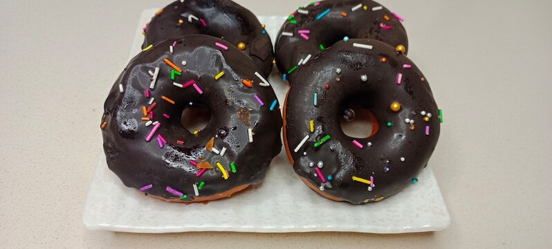 assorted donuts with chocolate frosted, pink glazed and sprinkles donuts. Donuts in hand or tray
