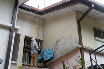 Painter worker adding undercoat foundation paint onto wall with roller at residential building in renovation