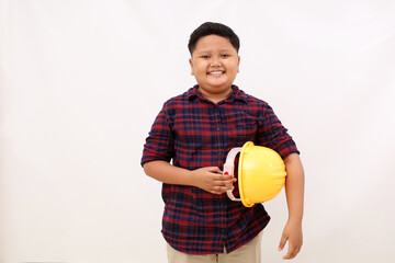 Happy asian boy standing while carrying engineer helmet. Kid's aspirations concept. Isolated on white background