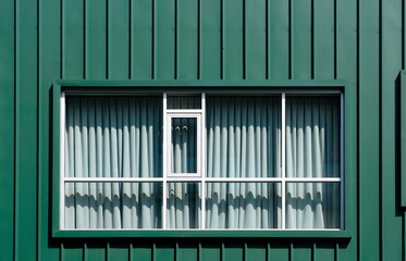Rectangular window with closed curtain on green building facade