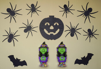 Scary Halloween figurines stand on a light background in close-up, behind hangs terrible pumpkin, spiders and bats. Cute character in monster costume. Halloween decorations