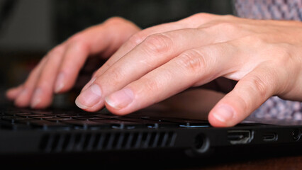 Fingers typing on laptop keyboard close-up. Work at the computer, IT sphere, development or remote online work. Side view