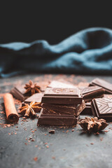 Dark chocolate bar pieces on dark background with grated chocolate and spices, pile chunks of broken chocolate