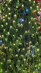 Closeup branches of coniferous tree decorated with glittering balls and shiny garland. Selective focus. Perfect festive content for stories background, vertical banner.