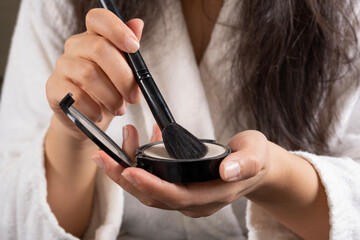 Holding tonal powder, caucasian woman's hand holding tonal powder. Morning skin care and make up routine. Close up image of girl using make up brush, wearing bathrobe getting ready for the day.
