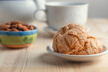 Close up view of two pardulas on a white plate with a white cup, almond on a little plate and white teapot over a wooden table