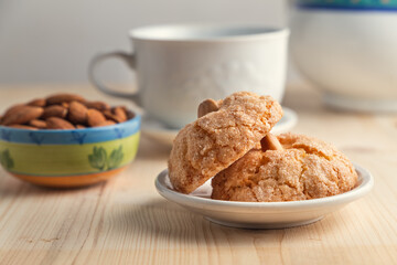 Two pardulas on a white plate with a white cup, almond on a little plate and white teapot over a wooden table