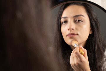 Applying makeup, beautiful millennial woman applying makeup. Holding and using brush for powder,...
