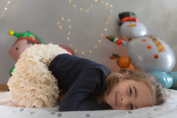 Cute little girl lying on the play mat with kind expression. Christmas balloon and lights...