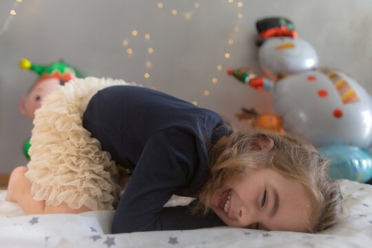 Cute little girl lying on the play mat with funny expression. Christmas balloon and lights decoration in the background