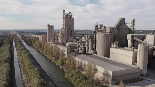 Traveling aerial view with drone in a cement industrial plant.  Cement manufacturing next to a lake. Industrial landscape