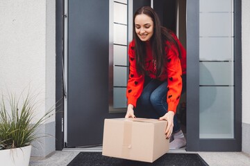 Smiling woman in Christmas spirit picking up a cardboard box at the front door