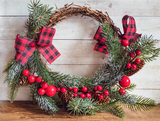 Fototapeta na wymiar Christmas wreath from pine and spruce twigs with cones, berries and red ribbon bow on wooden background 