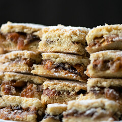 Layer pie with dried fruits and nuts. Shortbread with filling. Homemade family baking. Dessert is cut into pieces, laid out in pile. Close-up. Soft focus. Dark background.
