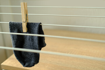 close-up of one dark gray men's sock hangs lonely on wire room dryer, home chores concept, missing...