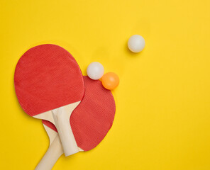 Pair of wooden tennis rackets for ping pong and plastic balls on a yellow background