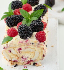 Baked meringue roll with cream and fresh fruits on a white wooden board, delicious dessert