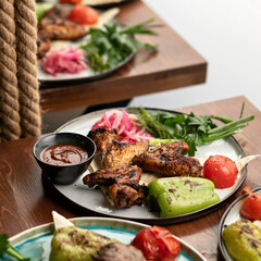 Meat with garnish. Chicken wings with grilled vegetables and sauce on a plate. Dish on a wooden table. Soft focus.
