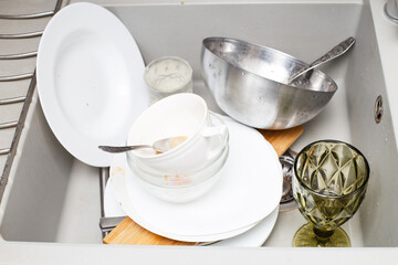 Pile of dirty dishes like plates, cutlery in the grey modern granite sink in the kitchen