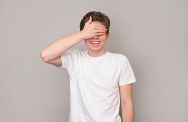 Young cheerful man covering eyes with hand anticipating surprise.