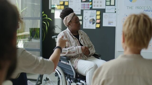 African American female business coach in wheelchair answering questions of audience while giving corporate training in office