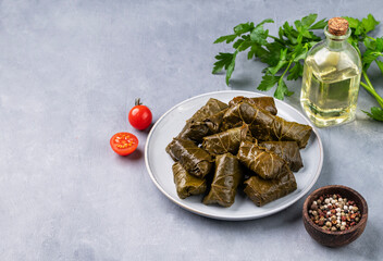 Dolma. Stuffed grape leaves (traditional Caucasian, Turkish, Greek cuisine) on a blue plate with fresh herbs on a light background with olive oil, tomato and pepper.