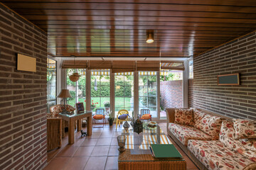A conservatory overlooking a backyard with gardens and grass and wicker and rattan furniture