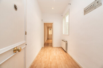 hallway of a house with all the walls painted plain white, a fuse box and a long corridor