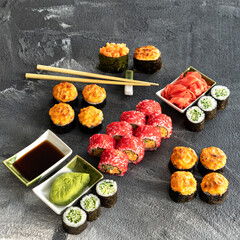 Sushi rolls set with wasabi soy sauce and ginger. Sushi chopsticks. Japanese cuisine. Baked rolls, vegetarian cucumber maki, caviar rolls. Dark gray background.Copy space. View from above. High