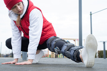 Woman wearing knee brace or orthosis after leg surgery working out in the park