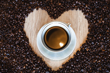 A cup of hot aromatic coffee in a saucer, against the background of scattered coffee beans in the...
